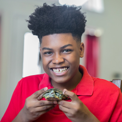 Teenage boy smiles while playing with pet turtle
