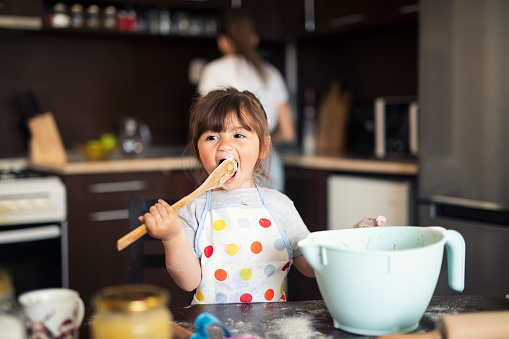 Cute little girl baking at home with mom, the little cook eats from the mixture