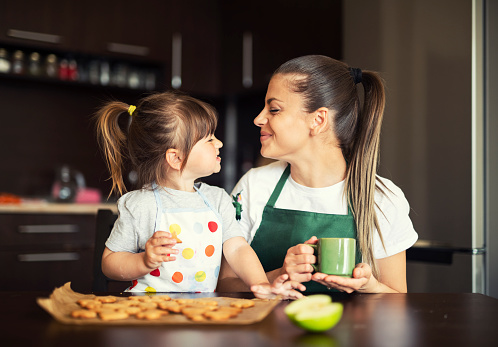 Happy family with baked cookies, mother and daughter having fun and eating fresh hot cookies