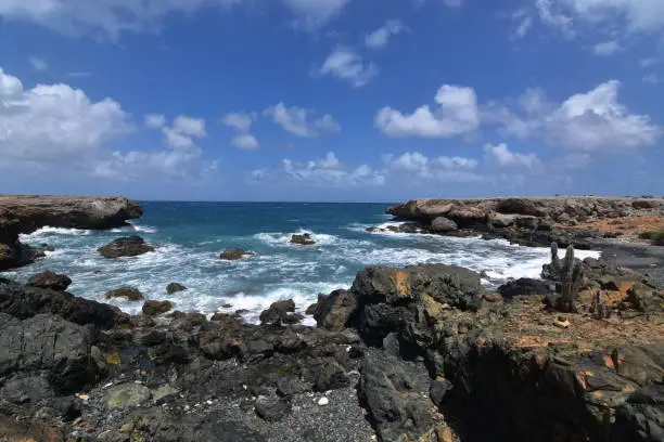 A scenic look on Aruba's black sand beach with rugged lava rocks.