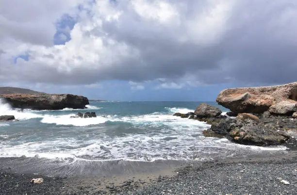 Pretty view of Aruba's black sand stone beach with waves lapping the shore.