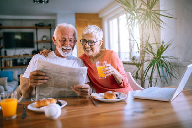 gioiosa coppia senior che legge giornali mentre mangia dessert - 60s senior adult breakfast cheerful foto e immagini stock