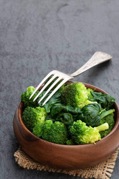 gedämpfte frische brokkoli mit spinat auf schwarzem steingrund - brokkoli stock-fotos und bilder
