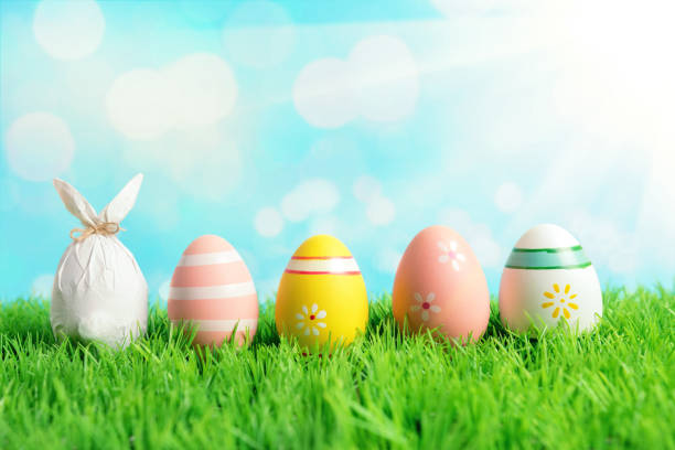 istock Easter egg wrapped in a paper in the shape of a bunny with colorful Easter eggs on green grass. Spring holidays concept. 1142674561