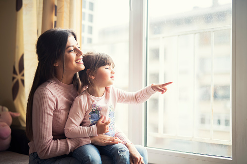 Cropped shot of a mother and her adorable little daughter looking out the window at home