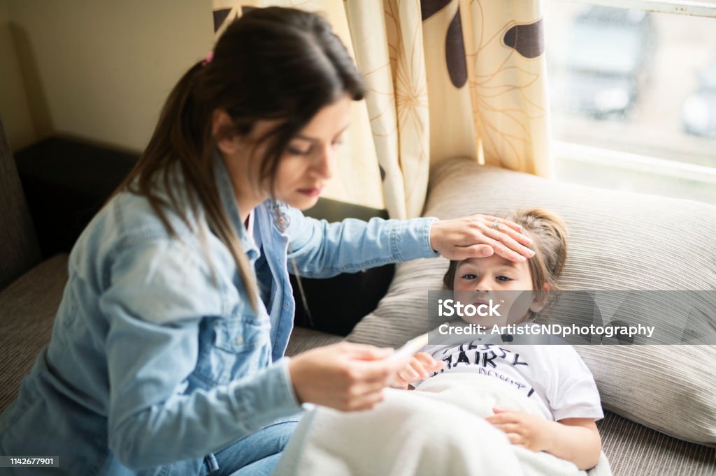 Mother checking on sick daughter laying in bed Mother checking temperature on sick daughter laying in bed Child Stock Photo