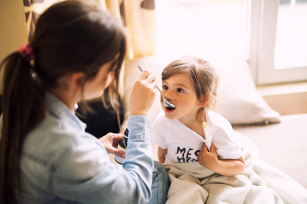 mother giving daughter medicine - offspring child lying on back parent imagens e fotografias de stock