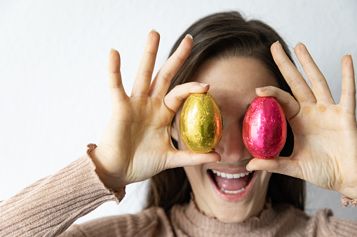 Woman holding golden and red chocolate easter eggs in front of her eyes