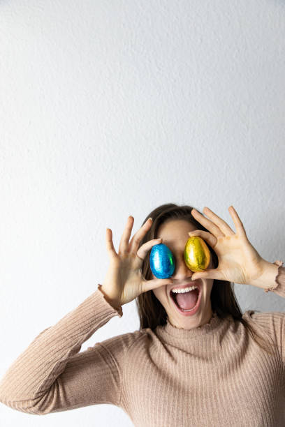 woman holding blue and golden chocolate easter eggs in front of her eyes - spring happiness women latin american and hispanic ethnicity imagens e fotografias de stock