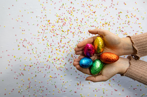 Woman hands holding colorful chocolate easter eggs with white background and colorful blurred confetti