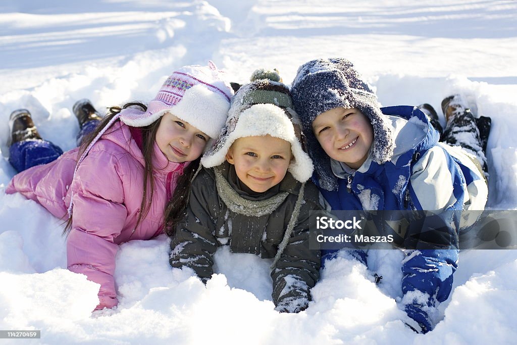 Tre bambini che giocano nella neve fresca - Foto stock royalty-free di Affettuoso