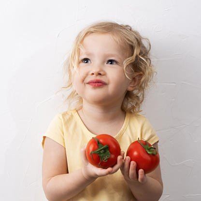 Little curly girl with tomatoes on a white background. Portrait.