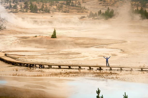 Woman waving from Norris Geyser Basin Yellowstone Park Woman viewed from afar standing on the boardwalk and waving with open arms at Norris Geyser Basin. norris geyser basin photos stock pictures, royalty-free photos & images