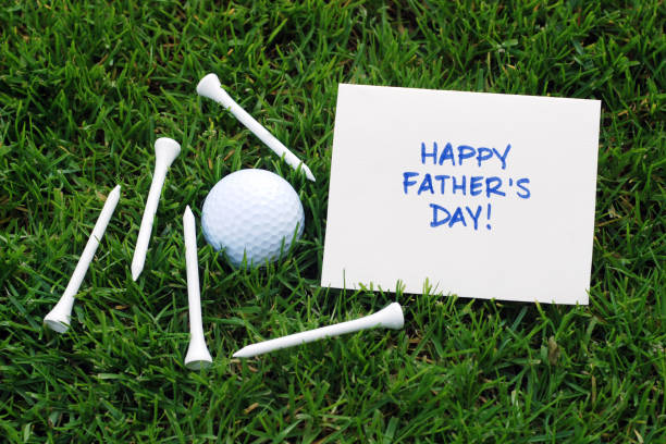 Closeup of a golf ball and tees on grass with a notecard reading Happy Father's Day.