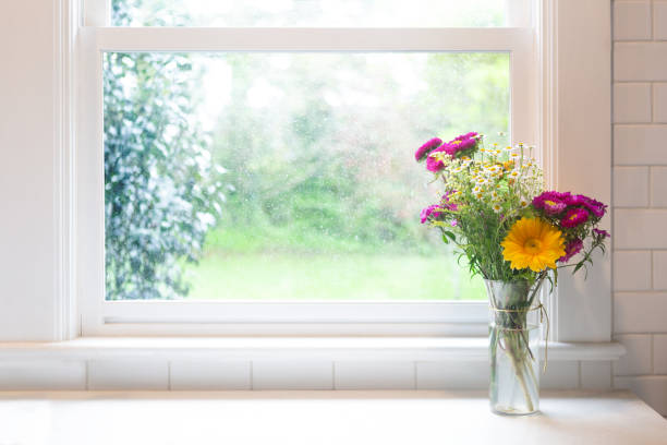 Bouquet of flowers by window, high key, in glass jar with copy space. Bright and airy in modern farmhouse kitchen