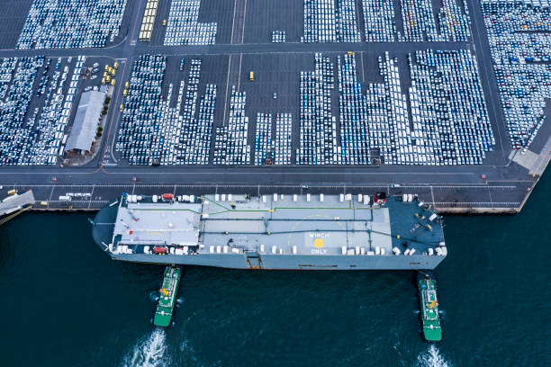 View over the vehicle terminal in the port of Southampton in the United Kingdom. A large vehicle transport ship has moored at the pier. Many vehicles are ready for loading.