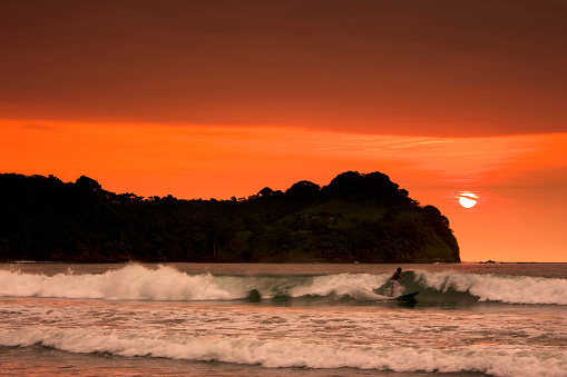 A young fit athlete running a wave surfing with a beautiful sunset over the sea and colorful clouds in Mompiche, Ecuador