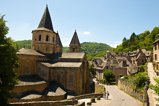 Conques, France-06 14 2014:People walking in the street of the medieval village of Conques, and admiring the Sainte-Foy Abbey-Church, located in Aveyron département, France.The Abbey Church of Saint Foy was added to the UNESCO World Heritage Sites in 1998, as part of the World Heritage Sites of the Routes of Santiago de Compostela in France.