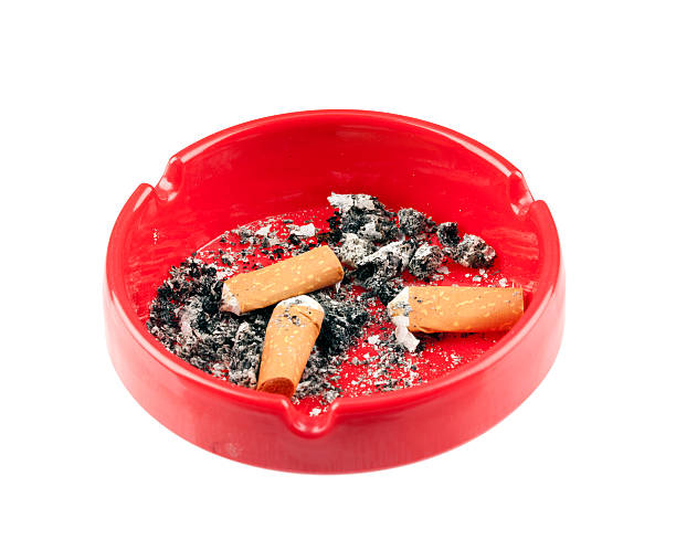 Cigarettes in pack and in ashtray are on the nightstand on the foreground. The bed is on the background. Smoking in bed conception