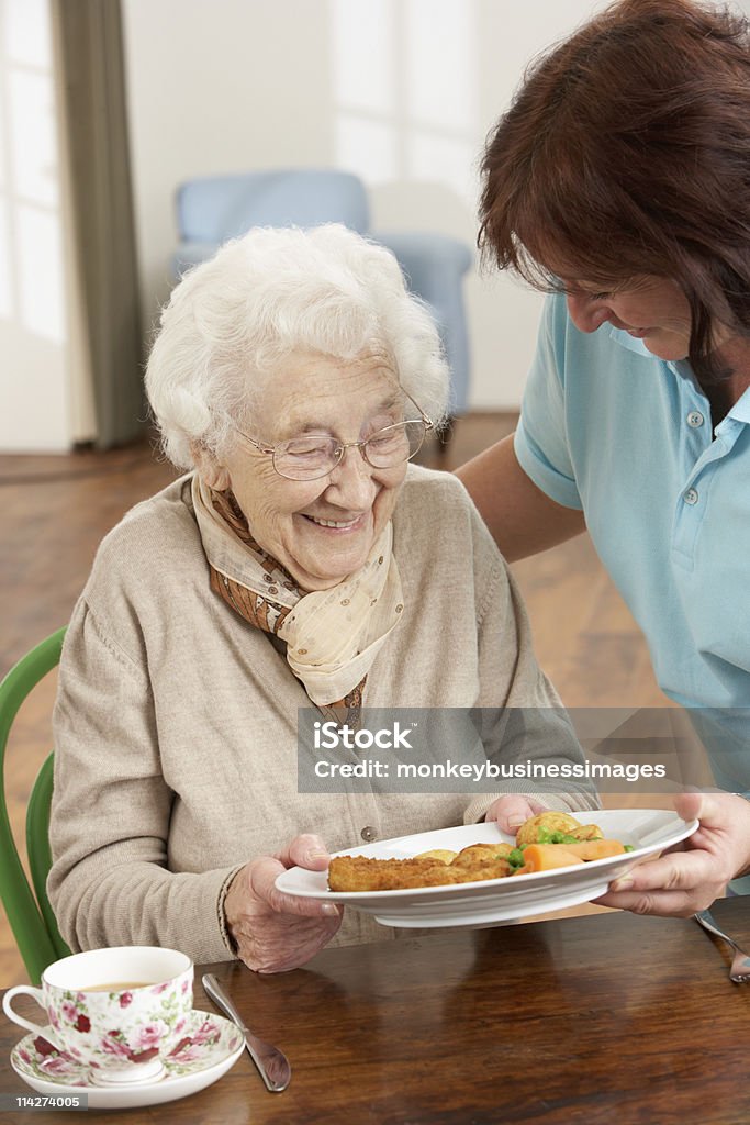 Starszy kobieta serwowane posiłki przez opiekuna jest - Zbiór zdjęć royalty-free (Senior)