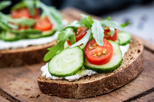 Healthy food rye bread with cream cheese, cucumber, tomato and arugula. Closeup view