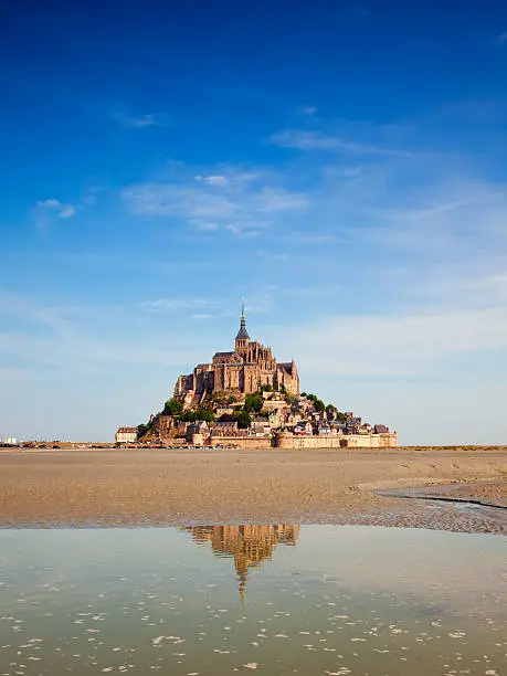 the famous Mont Saint Michel on a summer morning at ebbtide, partially reflected in the water