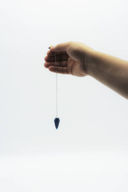 istock Pendulum dowsing on an isolated white background with an blue crystal and colored chakra stones. 1142750065