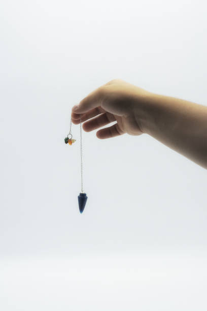 istock Pendulum dowsing on an isolated white background with an blue crystal and colored chakra stones. 1142750596