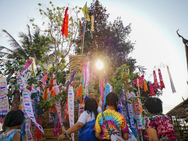 a família tailandesa polvilha a areia e coloc as bandeiras vibrantes do papel da cor amarradas às filiais em um castelo coberto de vime tradicional da areia no último dia do festival budista tailandês famoso de songkran do ano novo, em um templo budist - true thailand classic - fotografias e filmes do acervo