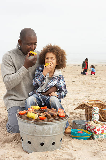 Young family enjoying barbecue on the sandy beach Young Family Enjoying Barbeque On Winter Beach family bbq beach stock pictures, royalty-free photos & images