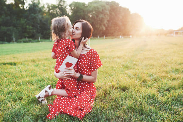 мать, держащая бумажную книгу и девочку в руках и дать ей поцелуй - heart shape grass paper green стоковые фото и изображения