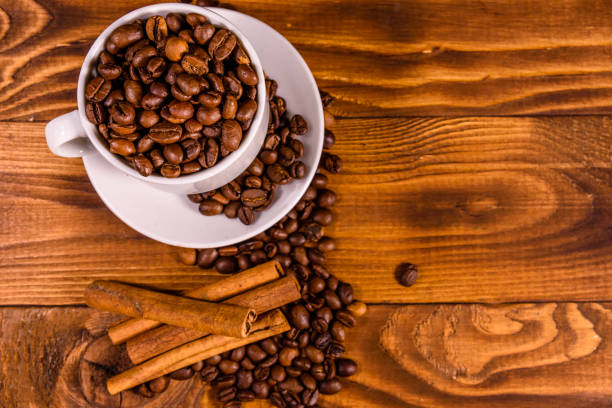 istock White cup filled with coffee beans and cinnamon sticks on wooden table. Top view 1142764706