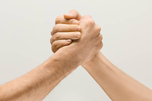 Two male hands competion in arm wrestling isolated on grey studio background Friends greetings sign or disagreement. Two male hands competion in arm wrestling isolated on grey studio background. Concept of standoff, support, friendship, business, community, strained relations. gripping stock pictures, royalty-free photos & images