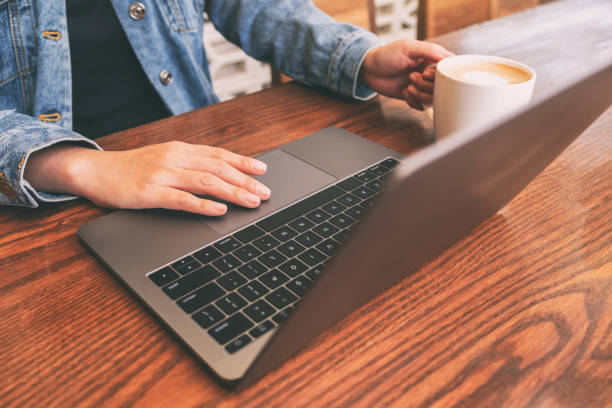 istock Closeup image of a woman using and touching on laptop touchpad on wooden table while drinking coffee 1142771113