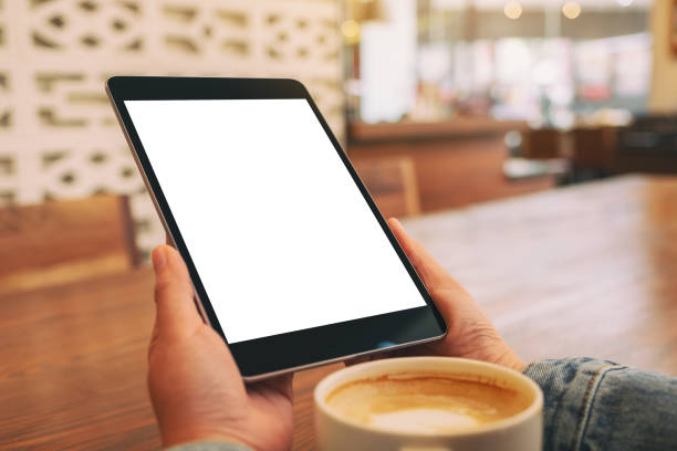 istock Mockup image of hands holding black tablet pc with blank white screen with coffee cup on wooden table 1142771623