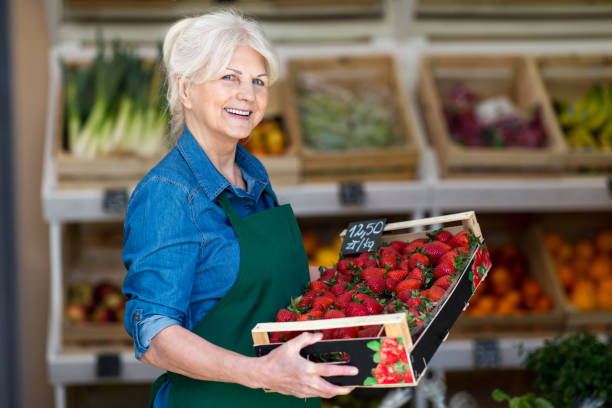 유기농 농산물가 게에서 신선한 딸기가 있는 숍 어시스턴트 홀딩 박스 - supermarket sales clerk grocer apron 뉴스 사진 이미지