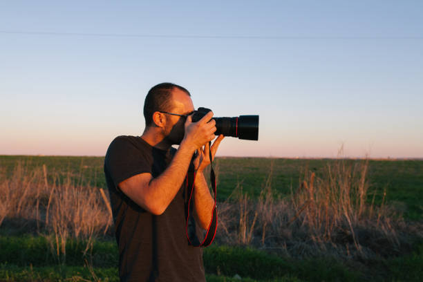 istock Man Holding Camera While Standing On Field Against Sky During Sunset 1142780667