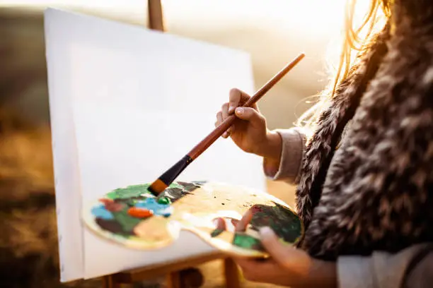 Close up of unrecognizable girl making a painting during autumn day in nature.