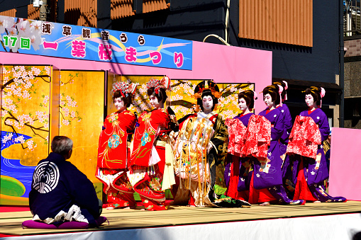 Tokyo, Japan-April 13, 2019:
Oirans' stage performance, entertaining their guest (a man on the left-hand corner), on one of the streets in Asakusa, Tokyo. The woman with very elaborate kimono is Tayu, the highest-ranked Oiran.
Oiran was a profession which flourished during Edo period (1600-1868) of Japan and was one of the popular figures in the woodblock prints. Although it has since died out, the Oiran tradition has survived even up to today in the form of parade and local entertainment in some parts of Japan. Oiran was, if I put in a nutshell, high class Geisha girls of those days. Yoshiwara near Asakusa was one of such most famous places and the parade and stage performance have been taking place on the second Saturday of April each year, attracting a huge crowd.
The highest-ranked Oiran was called Tayu, who wear very elaborate silk kimono weighing about 20 kilograms. She wears about 15 cm high Geta (clogs) and walks in a special style called Soto-Hachi-Monji (outside 8 letter), as if she is drawing letter “8” by her feet, placing her hand on the shoulder of an accompanying man to keep her balance.