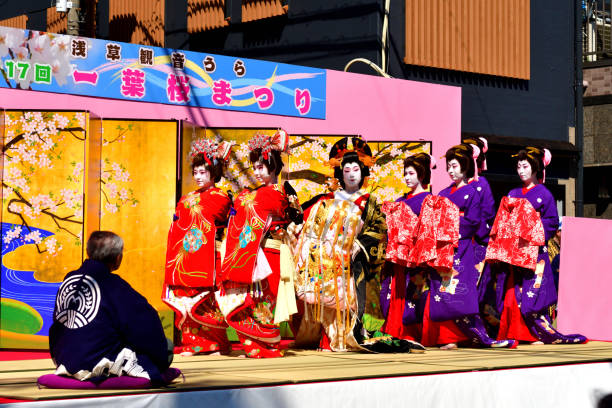 Asakusa Oiran Dochu (Parade): Parade and Stage Performance in Tokyo Tokyo, Japan-April 13, 2019:
Oirans' stage performance, entertaining their guest (a man on the left-hand corner), on one of the streets in Asakusa, Tokyo. The woman with very elaborate kimono is Tayu, the highest-ranked Oiran.
Oiran was a profession which flourished during Edo period (1600-1868) of Japan and was one of the popular figures in the woodblock prints. Although it has since died out, the Oiran tradition has survived even up to today in the form of parade and local entertainment in some parts of Japan. Oiran was, if I put in a nutshell, high class Geisha girls of those days. Yoshiwara near Asakusa was one of such most famous places and the parade and stage performance have been taking place on the second Saturday of April each year, attracting a huge crowd.
The highest-ranked Oiran was called Tayu, who wear very elaborate silk kimono weighing about 20 kilograms. She wears about 15 cm high Geta (clogs) and walks in a special style called Soto-Hachi-Monji (outside 8 letter), as if she is drawing letter “8” by her feet, placing her hand on the shoulder of an accompanying man to keep her balance. geta sandal photos stock pictures, royalty-free photos & images