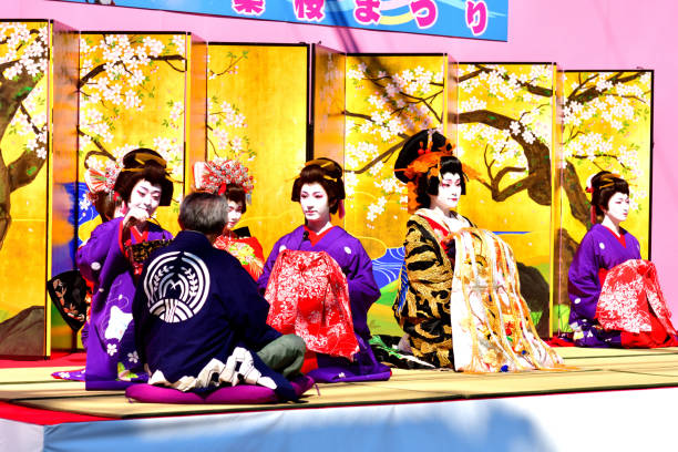 Asakusa Oiran Dochu (Parade): Parade and Stage Performance in Tokyo Tokyo, Japan-April 13, 2019:
Oirans' stage performance, entertaining their guest (a man on the left-hand corner), on one of the streets in Asakusa, Tokyo. The woman with very elaborate kimono is Tayu, the highest-ranked Oiran.
Oiran was a profession which flourished during Edo period (1600-1868) of Japan and was one of the popular figures in the woodblock prints. Although it has since died out, the Oiran tradition has survived even up to today in the form of parade and local entertainment in some parts of Japan. Oiran was, if I put in a nutshell, high class Geisha girls of those days. Yoshiwara near Asakusa was one of such most famous places and the parade and stage performance have been taking place on the second Saturday of April each year, attracting a huge crowd.
The highest-ranked Oiran was called Tayu, who wear very elaborate silk kimono weighing about 20 kilograms. She wears about 15 cm high Geta (clogs) and walks in a special style called Soto-Hachi-Monji (outside 8 letter), as if she is drawing letter “8” by her feet, placing her hand on the shoulder of an accompanying man to keep her balance. oiran stock pictures, royalty-free photos & images