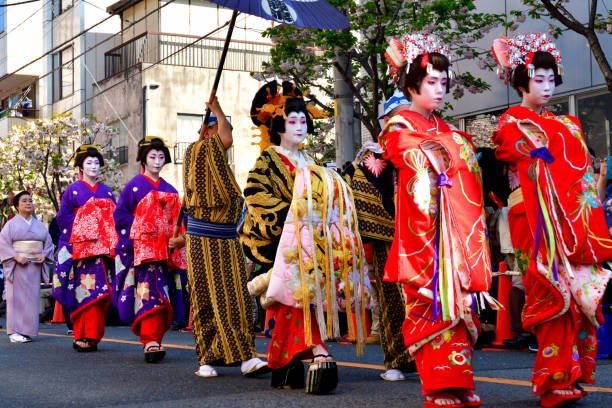 Asakusa Oiran Dochu (Parade): Parade and Stage Performance in Tokyo Tokyo, Japan-April 13, 2019:
Oirans' parade on the street of Asakusa after their stage performance in Asakusa, Tokyo. The woman under the umbrella with very elaborate kimono is Tayu, the highest-ranked Oiran.
Oiran was a profession which flourished during Edo period (1600-1868) of Japan and was one of the popular figures in the woodblock prints. Although it has since died out, the Oiran tradition has survived even up to today in the form of parade and local entertainment in some parts of Japan. Oiran was, if I put in a nutshell, high class Geisha girls of those days. Yoshiwara near Asakusa was one of such most famous places and the parade and stage performance have been taking place on the second Saturday of April each year, attracting a huge crowd.
The highest-ranked Oiran was called Tayu, who wear very elaborate silk kimono weighing about 20 kilograms. She wears about 15 cm high Geta (clogs) and walks in a special style called Soto-Hachi-Monji (outside 8 letter), as if she is drawing letter “8” by her feet, placing her hand on the shoulder of an accompanying man to keep her balance. oiran stock pictures, royalty-free photos & images