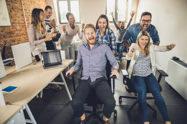 istock Young playful colleagues having fun while competing on chairs at casual office. 1142799677