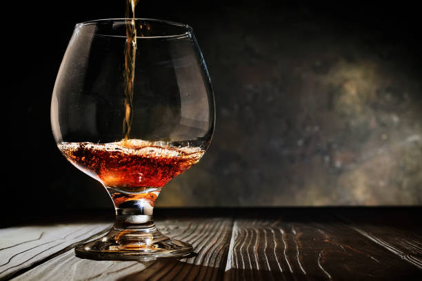 istock Cognac is poured into a glass on an old dark wooden background. Free copy space. Selective focus. 1142801183