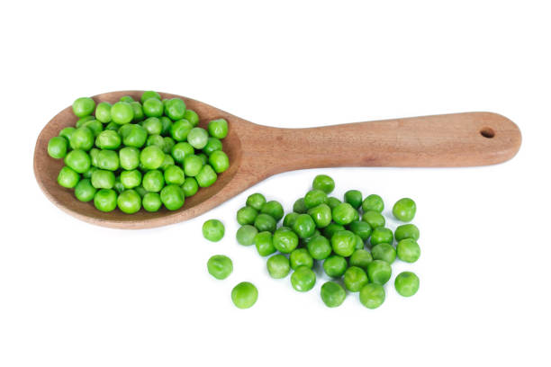 istock green peas on wooden spoon on white background. 1142801336