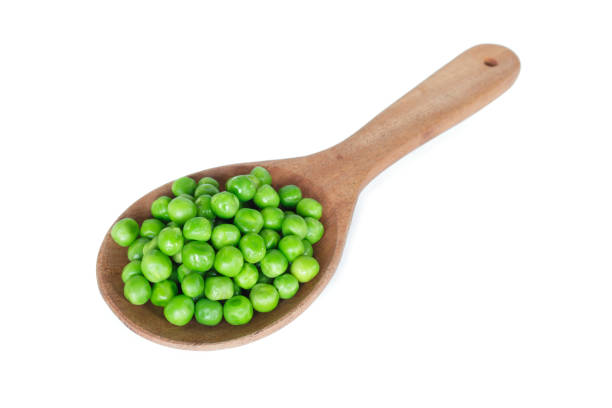 istock green peas on wooden spoon on white background. 1142802359