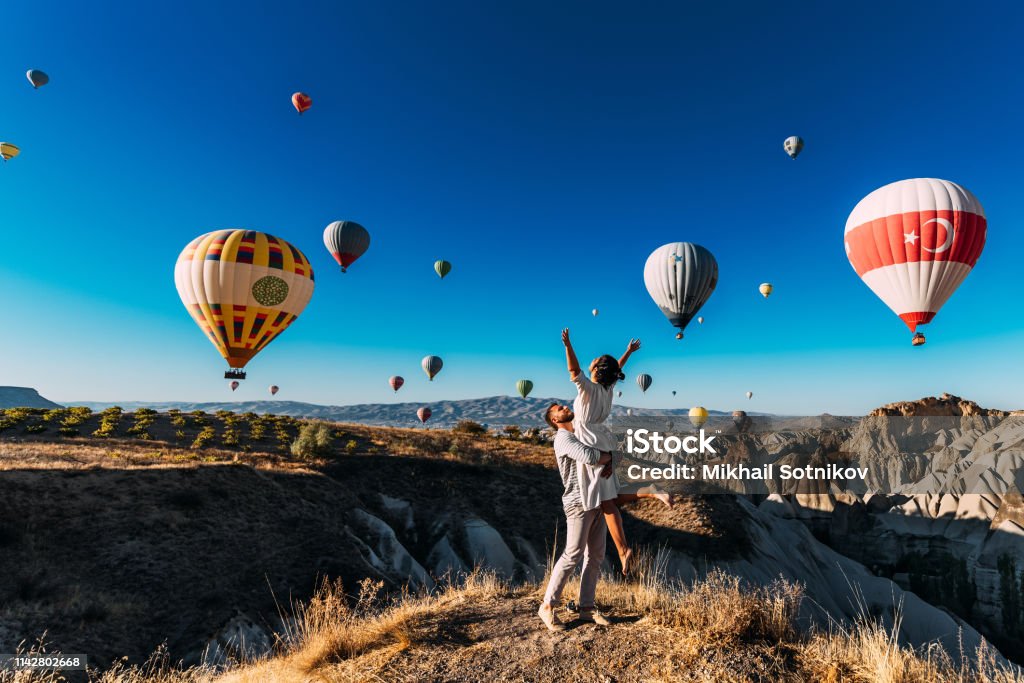 Wedding travel. Honeymoon trip. Couple in love among balloons. A guy proposes to a girl. Couple in love in Cappadocia. Couple in Turkey.  Man and woman traveling. Flying on balloons. Tourists Travel Stock Photo