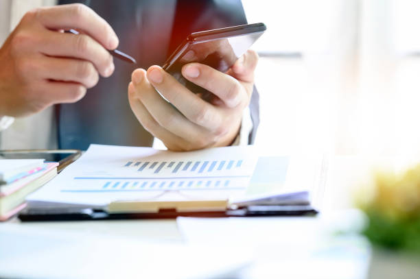 istock Closeup image of businessman using stylus working on mobile smartphone while sitting at office desk. Copy space. 1142804110