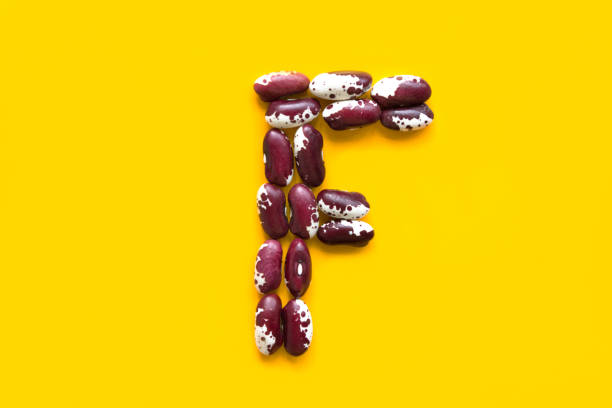 Capital letter F from dry uncooked red and white speckled beans legumes on bright yellow background. Creative food typography art poster. Symbol for folic acid. Health plant based meatless diet wholefoods letra mayúscula f de frijoles manchados rojos y blancos secos sin cocer sobre fondo amarillo brillante. cartel de arte creativo de comida creativa. símbolo de ácido fólico. el concepto de alimentos integrales de dieta sin carne basada en plantas de sal