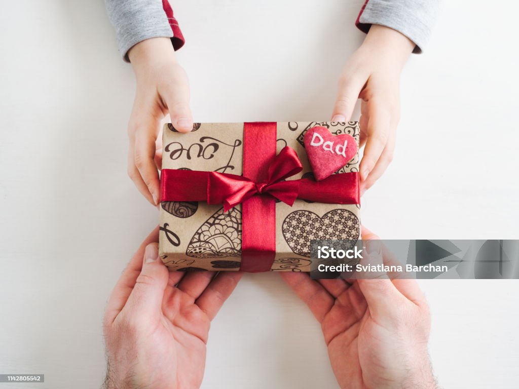 Child's hands and a beautiful gift box, Child's hands and adult man's hands, beautiful gift box, ribbon and glazed cookies on a white, wooden background. Top view, close-up. Preparing for the holidays Gift Stock Photo